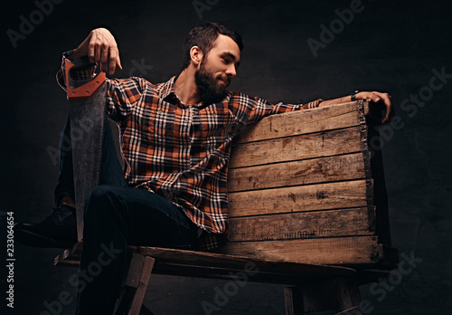 Worker, carpenter, handyman holding a saw in a studio, isolated on a dark background.