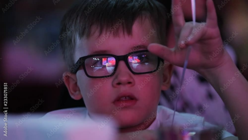 Close up seriously young pretty boy with glasses sitting looking blue light childhood candy lifestyle party child cute restaurant boy caucasian inside face portrait Close up seriously young pretty boy with glasses sitting looking blue light childhood candy lifestyle party child cute restaurant boy caucasian inside face portrait