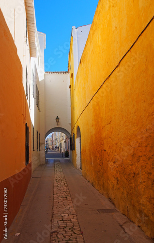 a long narrow alley in ciutadella town menorca with a bright yellow wall and archway at the end with a blue summer sky © Philip J Openshaw 