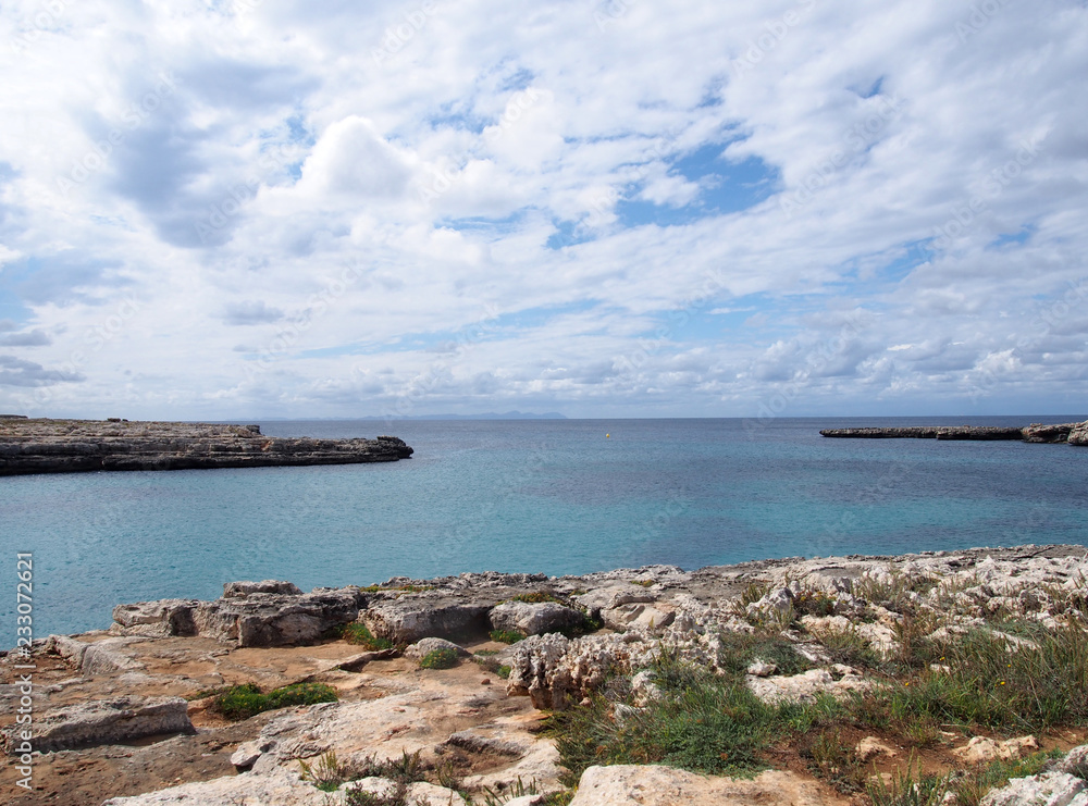 clifftop view of the cove at cale santandria in menorca with rocky shore and blue summer sea with white clouds