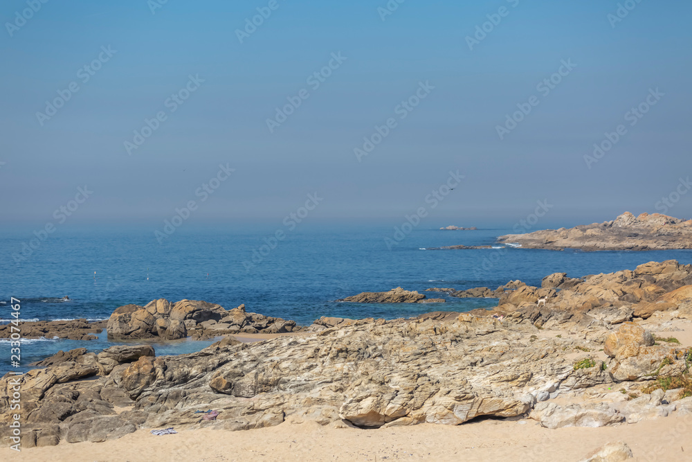 View of the atlantic ocean with sea and rocks with a person resting and a white dog, on the coast of Leca da Palmeira View of the atlantic ocean with sea and rocks with a person resting and a white dog, on the coast of Leca da Palmeira