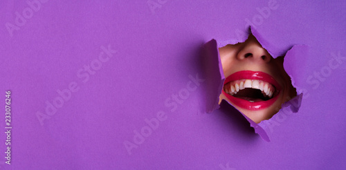 View of bright lips through hole in violet paper background. Make up artist, beauty concept. Cosmetics sale. Beauty salon advertising banner with copy space