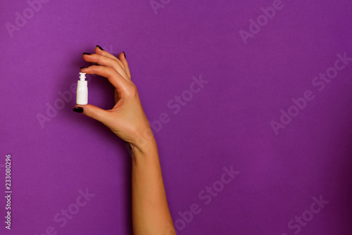 Female hands holding white cosmetic bottle on violet background. Banner. Skin care, pure beauty, body treatment concept