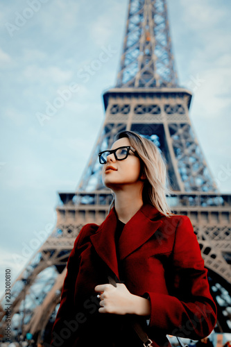 Style redhead girl in red coat and bag at parisian street with view at Eiffel tower in autumn season time
