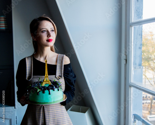 adult girl holding a cream cake with Eiffel tower on it near window
