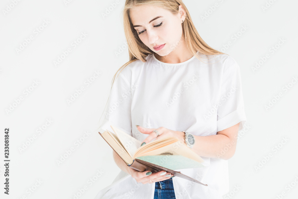 Portrait of a young stylish blonde girl in a white T-shirt and blue jeans reading a book on a white background Portrait of a young stylish blonde girl in a white T-shirt and blue jeans reading a book on a white background