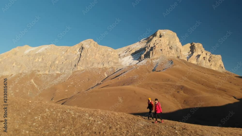 Aerial view of a two girls traveler with backpacks and cameras stroll through the hills between the epic rocks in the mountains. Girls photographers with their cameras at sunset Aerial view of a two girls traveler with backpacks and cameras stroll through the hills between the epic rocks in the mountains. Girls photographers with their cameras at sunset
