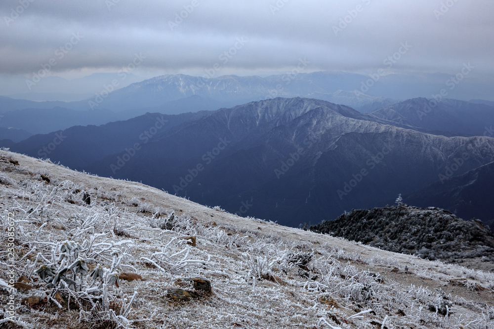 Mountain Landscape covered in Frost, Snow and Ice. Mountains above the clouds, haze and fog. Frigid cold atmosphere, frozen environment. Winter background, hiking trekking adventure. China Mountains