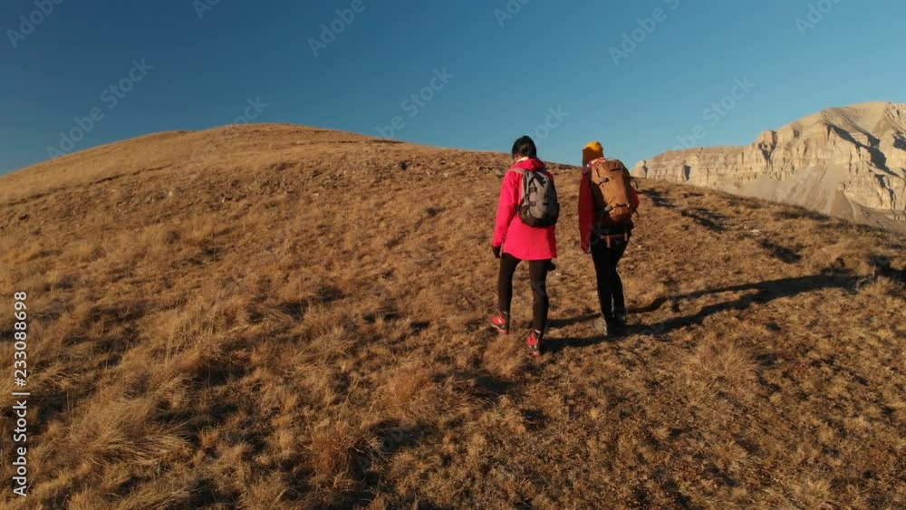 Aerial view of two girls traveler with backpacks and cameras go up the hill between the epic rocks in the mountains. Girls photographers with their cameras at sunset Aerial view of two girls traveler with backpacks and cameras go up the hill between the epic rocks in the mountains. Girls photographers with their cameras at sunset