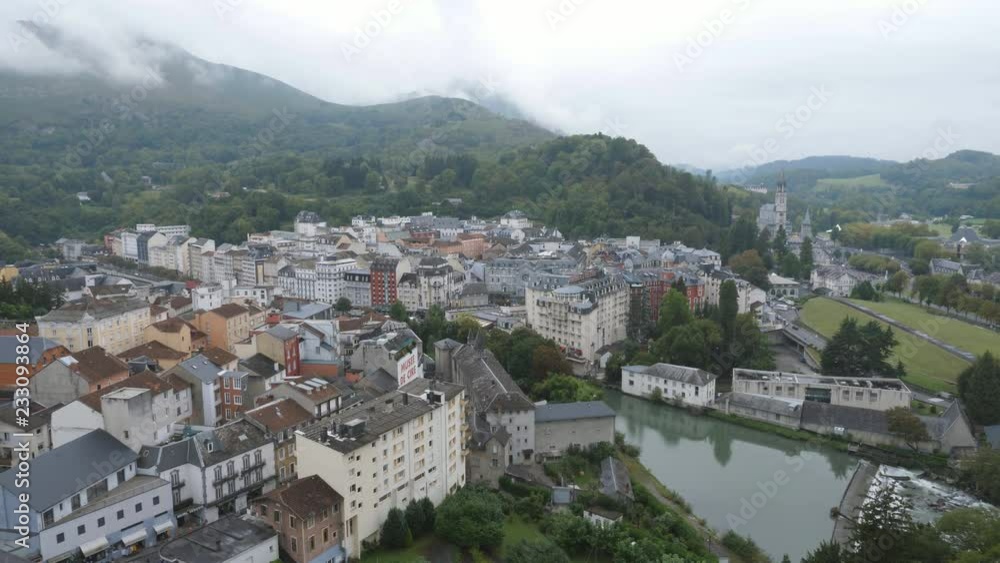 High angle view of Lourdes, France. Hotels and Gave de Pau river visible. Sanctuary of Our Lady of Lourdes, also known as the 'Domain' at right. Handheld shot with stabilized camera. High angle view of Lourdes, France. Hotels and Gave de Pau river visible. Sanctuary of Our Lady of Lourdes, also known as the 'Domain' at right. Handheld shot with stabilized camera.