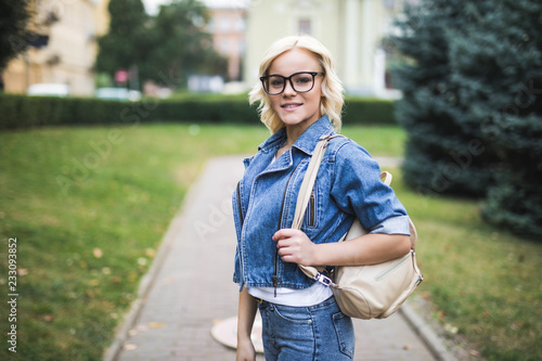 Young beauty woman in eyesglasses posing in the street with backpack, blonde hair, outdoor closeup portrait.