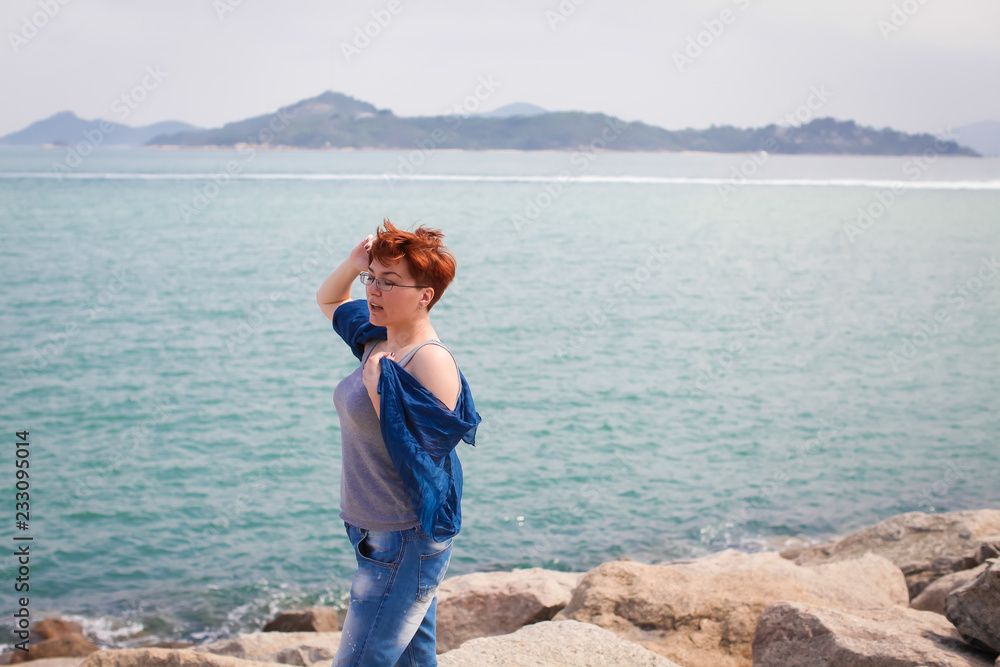 Adult caucasian women on rocky beach holding blue scarf in the air. Freedom concept