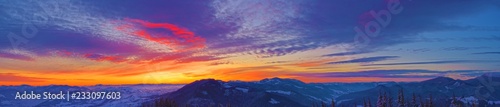 Wide panorama with beautiful sunrise in the winter Carpathians. Bright colorful sky. The mountains and the forest are covered with snow.