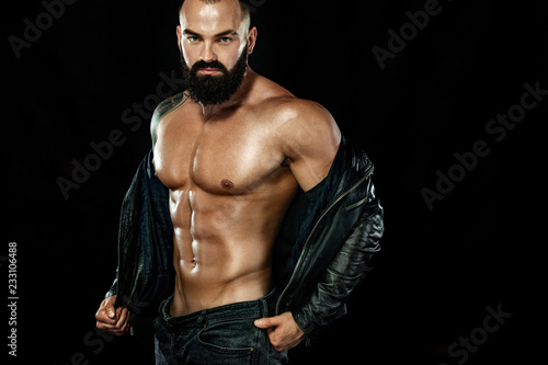 Men fashion concept. Close-up portrait of a brutal bearded man topless in a leather jacket. Athlete bodybuilder on black background. © Mike Orlov