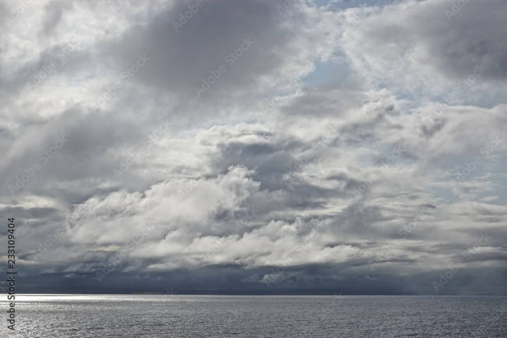 The sun pierces through gathering storm clouds over the Gulf of Alaska.