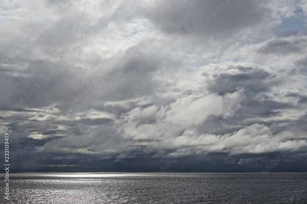 The sun pierces through gathering storm clouds over the Gulf of Alaska.