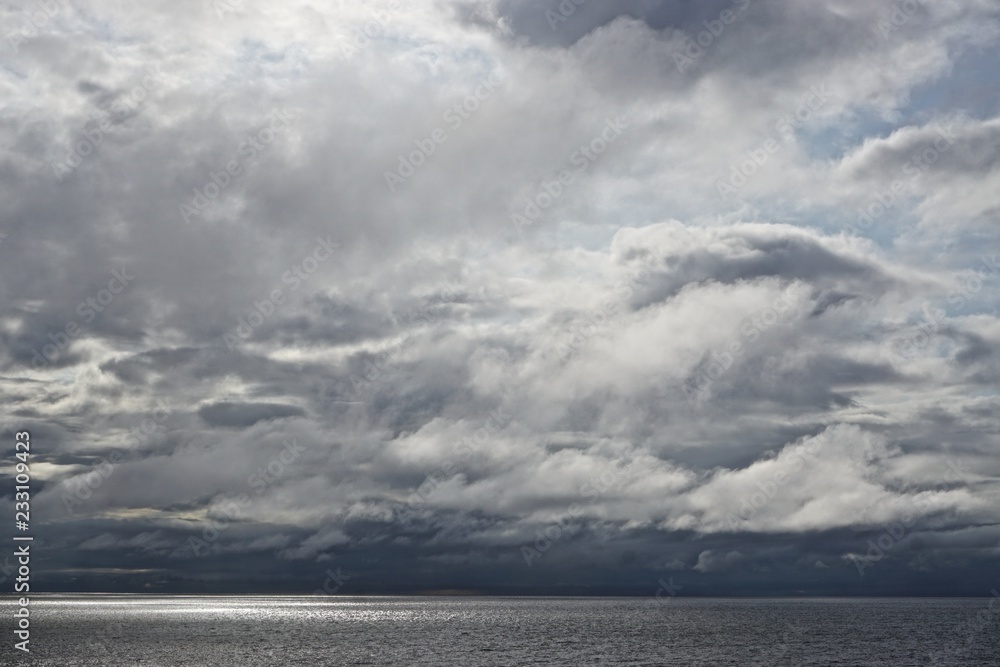 The sun pierces through gathering storm clouds over the Gulf of Alaska.