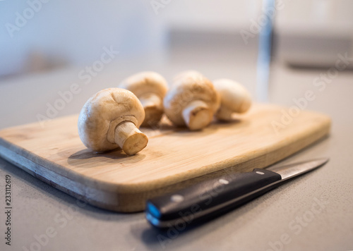 Whole white mushrooms on the wooden cutting board with the knife