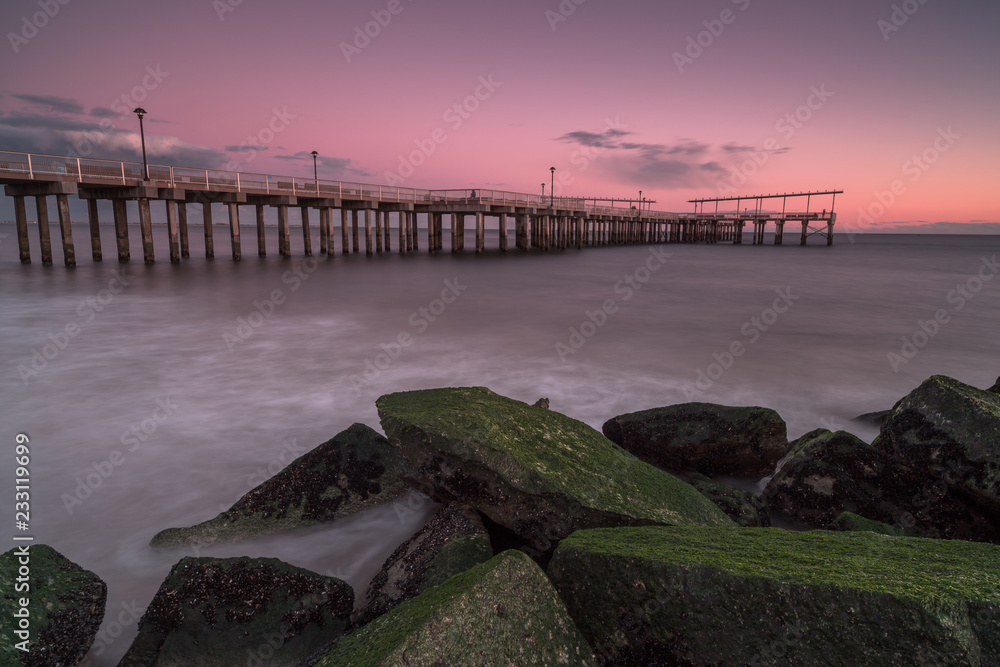 View on the pier from the sand beach with moss rocks at sunset,long exposure