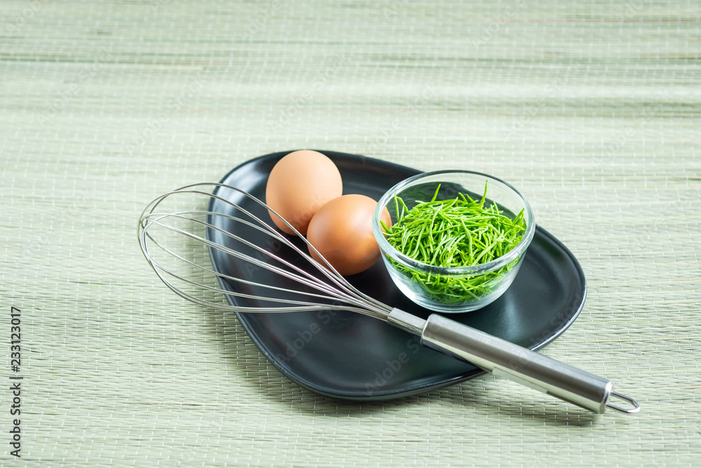 Acacia Pennata (Climbing Wattle) in small glass bowl with two eggs and a whisk on black plate Acacia Pennata (Climbing Wattle) in small glass bowl with two eggs and a whisk on black plate