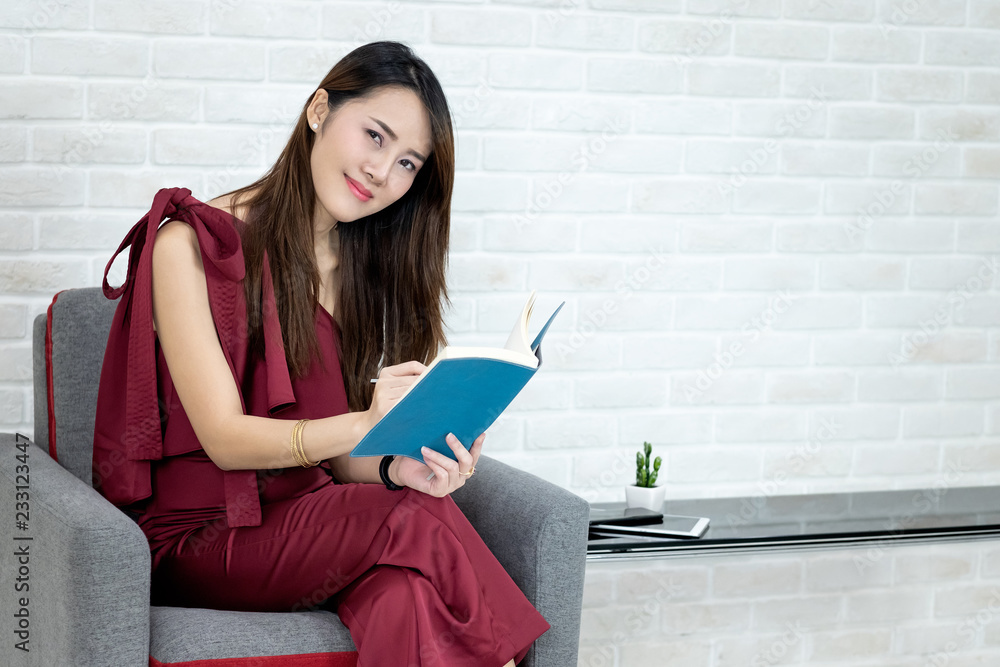 Portrait of beautiful young Asian business woman sitting and writing note in blue diary book Portrait of beautiful young Asian business woman sitting and writing note in blue diary book