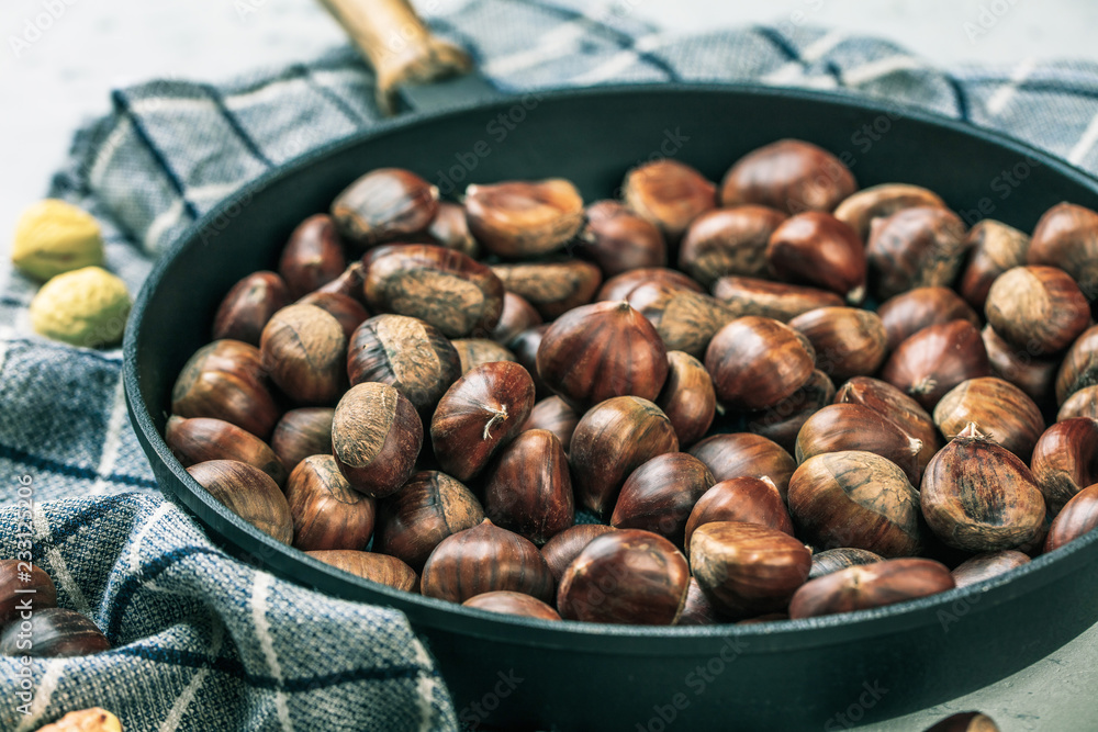 Obraz premium Roasted chestnuts served in chestnut pan on an old table