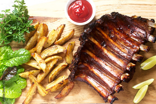 Homemade baked meat ribs served with french fries, herbs, lime and ketchup on a wooden board. Rustic style. photo