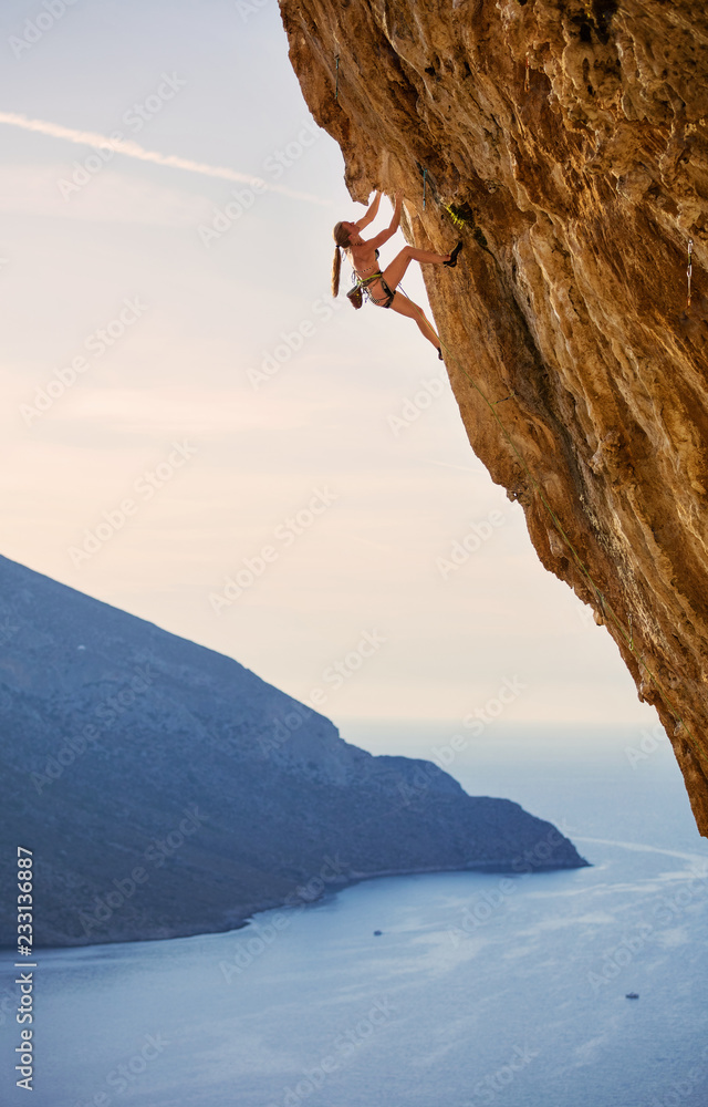 Young female rock climber on challenging route on cliff
