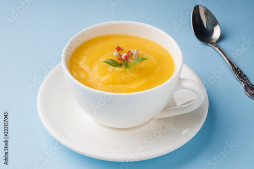 Pumpkin soup mashed with spices in a Cup on a blue background.