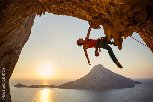 Male rock climber hanging with one hand on challenging route at sunset