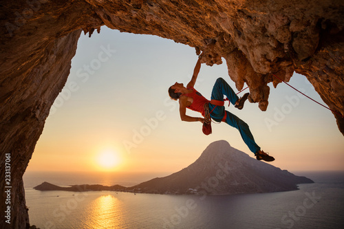 Male rock climber hanging with one hand on challenging route on cliff at sunset