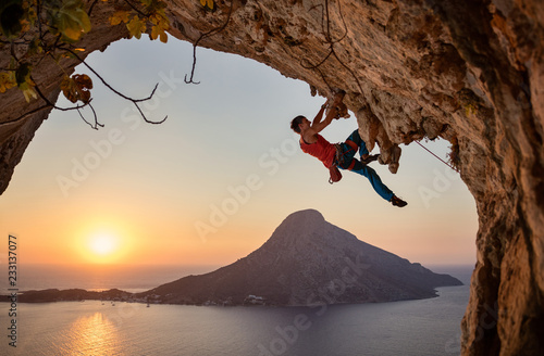 Male rock climber on challenging route on cliff at sunset