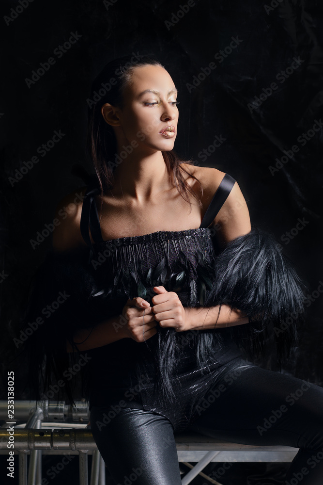 Low key portrait of pretty girl in fur vest and leather pants on dark background