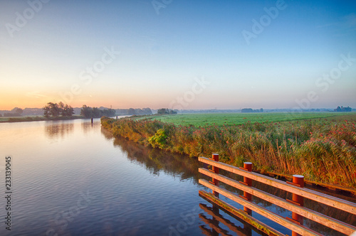 View at the Eempolder and the calm Eem river, shot against a clear blue sky at sunrise.