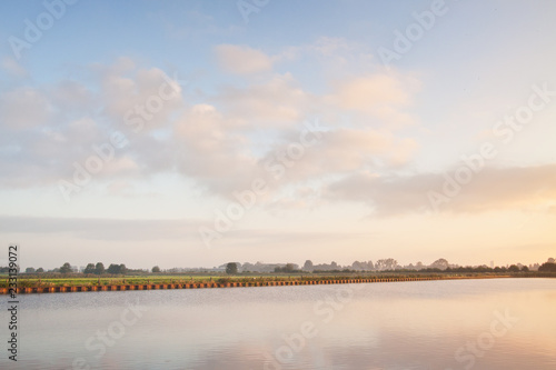 View at the Eempolder and the calm Eem river  shot against a clear blue sky at sunrise.