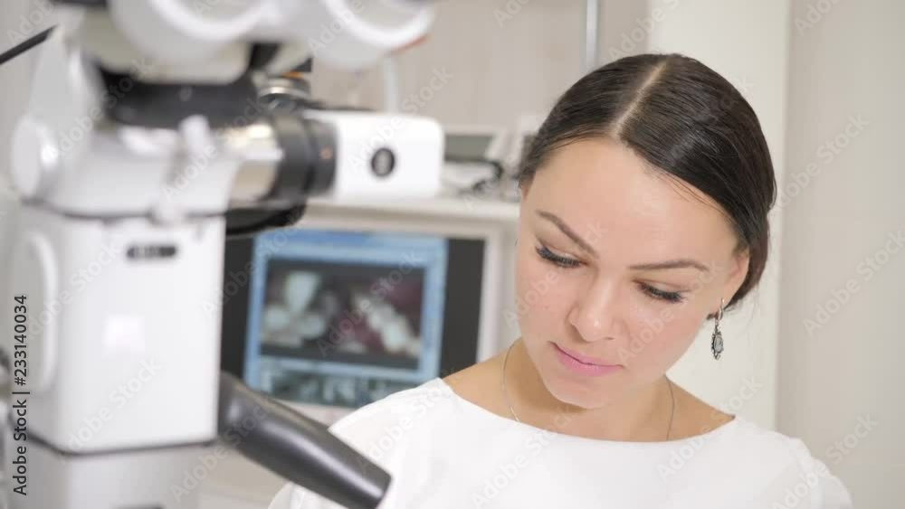 The dentist directs modern microscope to the patient. Beautiful woman doctor dentist. Young African American male patient at chair at dental clinic. Medicine, health, stomatology concept. The dentist directs modern microscope to the patient. Beautiful woman doctor dentist. Young African American male patient at chair at dental clinic. Medicine, health, stomatology concept.
