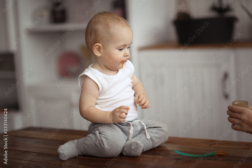 Mom feeds baby with spoon, cozy real interior Mom feeds baby with spoon, cozy real interior