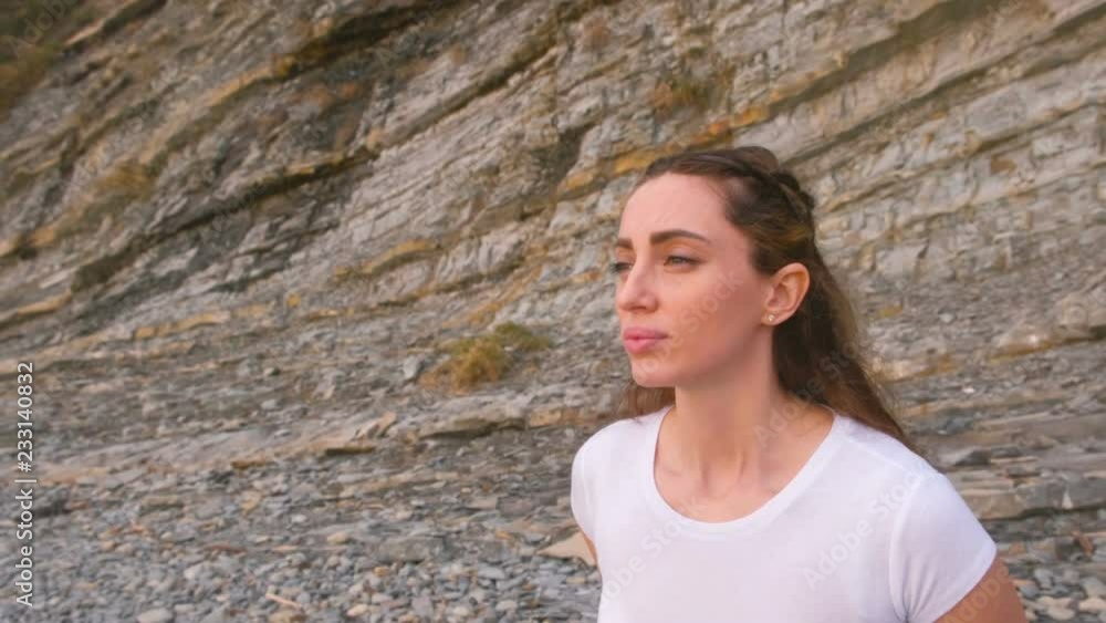 Girl is doing squats the bodyflex during breathing exercises on the rock background. Face close-up. Girl is doing squats the bodyflex during breathing exercises on the rock background. Face close-up.