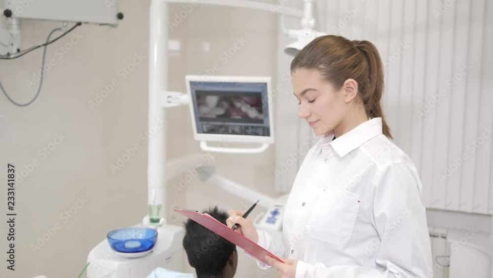 Beautiful woman doctor dentist. Young African American male patient at chair at dental clinic. Medicine, health, stomatology concept. dentist conducts inspection and concludes. looking into the camera Beautiful woman doctor dentist. Young African American male patient at chair at dental clinic. Medicine, health, stomatology concept. dentist conducts inspection and concludes. looking into the camera