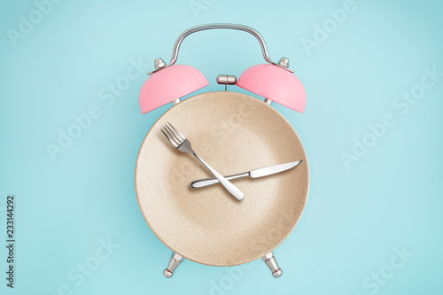 Alarm clock and plate with cutlery . Concept of intermittent fasting, lunchtime, diet and weight loss photo