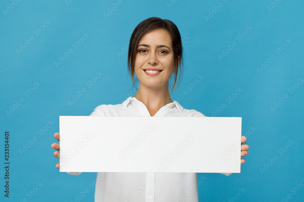 Businesswoman wearing white elegant shirt showing blank signboard against blue background Businesswoman wearing white elegant shirt showing blank signboard against blue background
