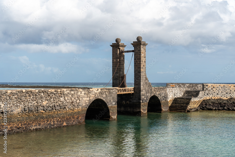 Sea landscape with an old stone bridge and a gate. Puente de las Bolas (Balls Bridge), landmark of Arrecife, the capital of Lanzarote, Spain.