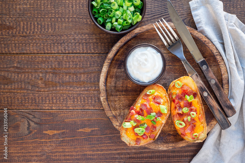 Baked loaded potato skins with cheddar cheese and bacon on a wooden plate, garnished with scallions and sour cream, horizontal, top view, copy space