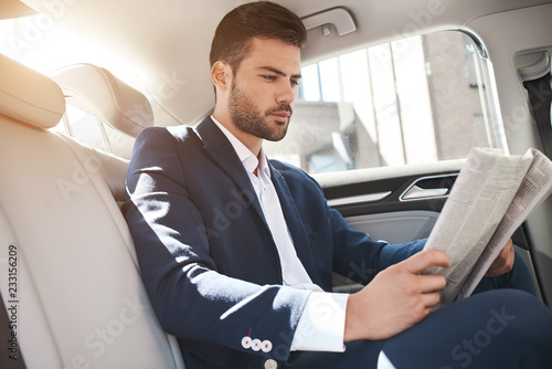Young stylish businessman reads newspaper on backseat of car © Friends Stock