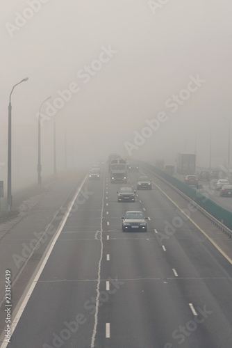 Dense fog and poor visibility on the road. Dangerous driving situations. View on highway traffic. Misty morning. Low visibility. Smoke on the road. Semi-trailer truck and cars driving trough the mist.