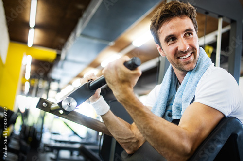 Young attractive adult man exercising and doing weight lifting at gym