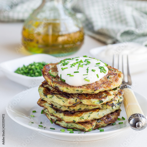 Vegetarian zucchini fritters or pancakes, served with greek yogurt and green onion on a white plate, square format