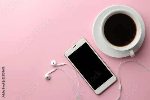 White smartphone with headphones and a cup of coffee on a bright pink background. view from above