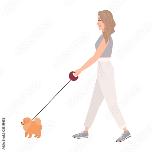 Smiling young woman dressed in casual clothing walking dog on leash