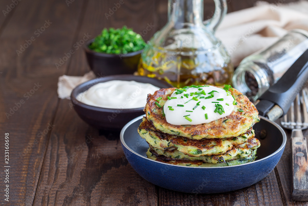 Vegetarian zucchini fritters or pancakes, served with greek yogurt and green onion, in little pan, horizontal, copy space